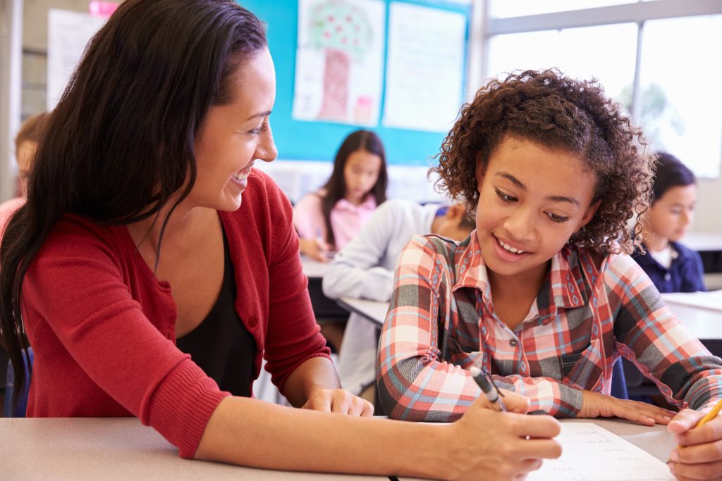 Teacher working with elementary school girl at her desk